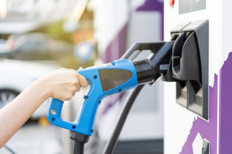 Unrecognizable Asian woman holding aa DC - CCS type 2 EV charging connector at EV charging station,